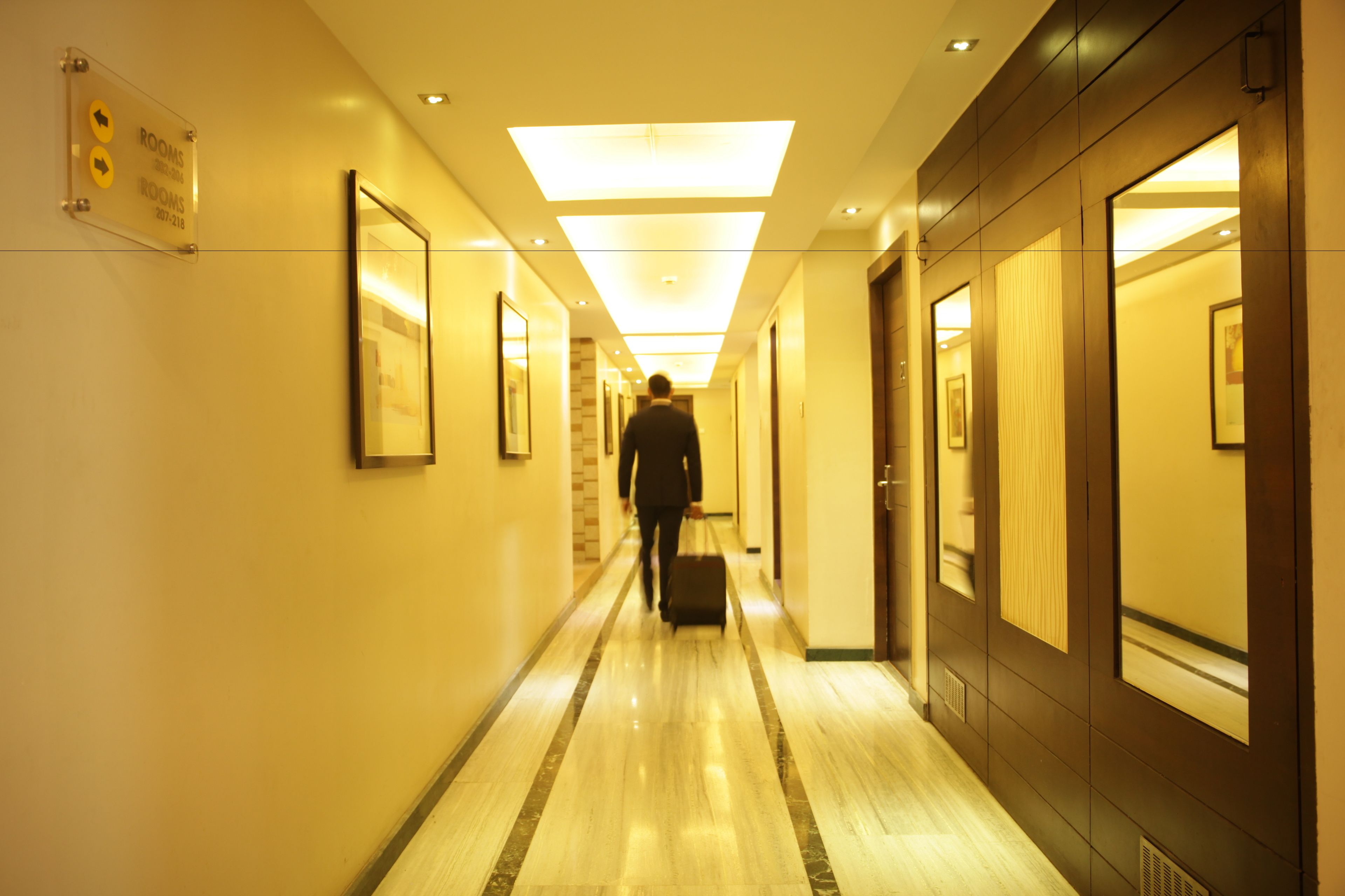 Een hotelgang met bewegwijzering, een man die een koffer voortduwt, en deuren aan de rechterkant.