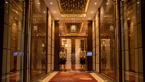 Un hall de hotel con alfombra roja, puertas de cristal y dos hombres de pie.