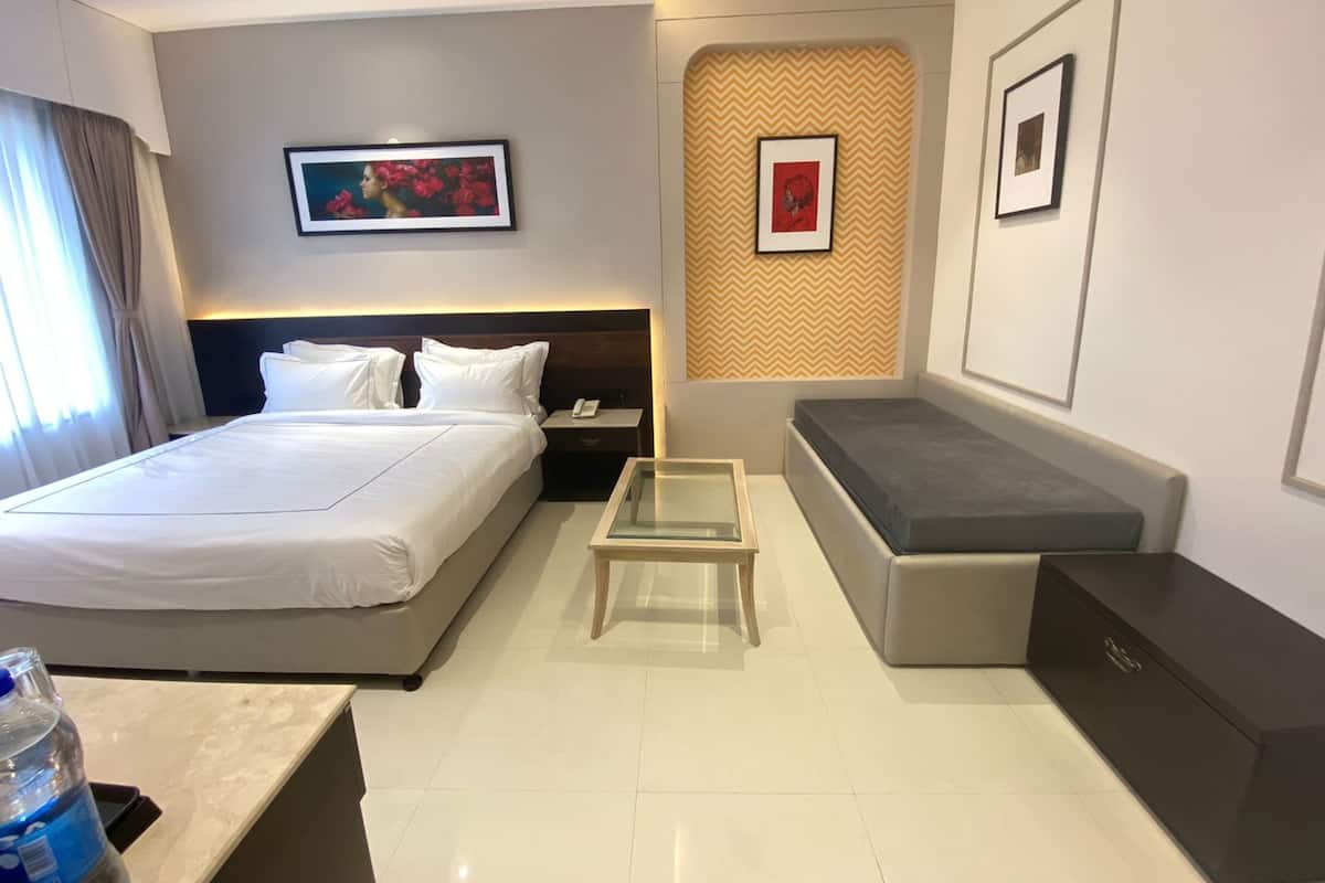 A hotel room with a bed, bedside table, a small seating area, and a wall with framed pictures.