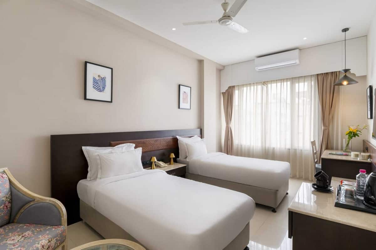 A hotel room with two beds, a desk, a chair, and a ceiling fan.
