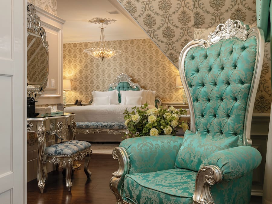 Une chambre à coucher avec un grand lit, une coiffeuse, une chaise et un lustre.