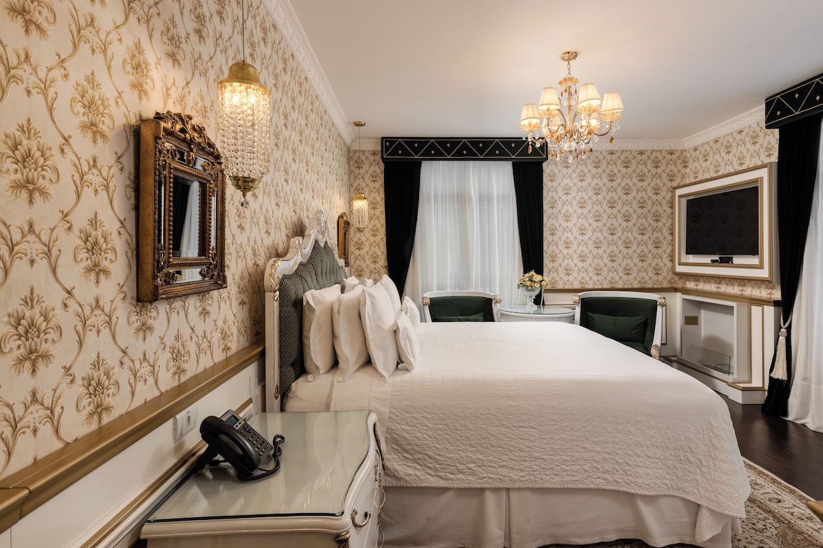 Ett hotellrum med en stor säng, ett skrivbord med en telefon, en tv och en kristallkrona.