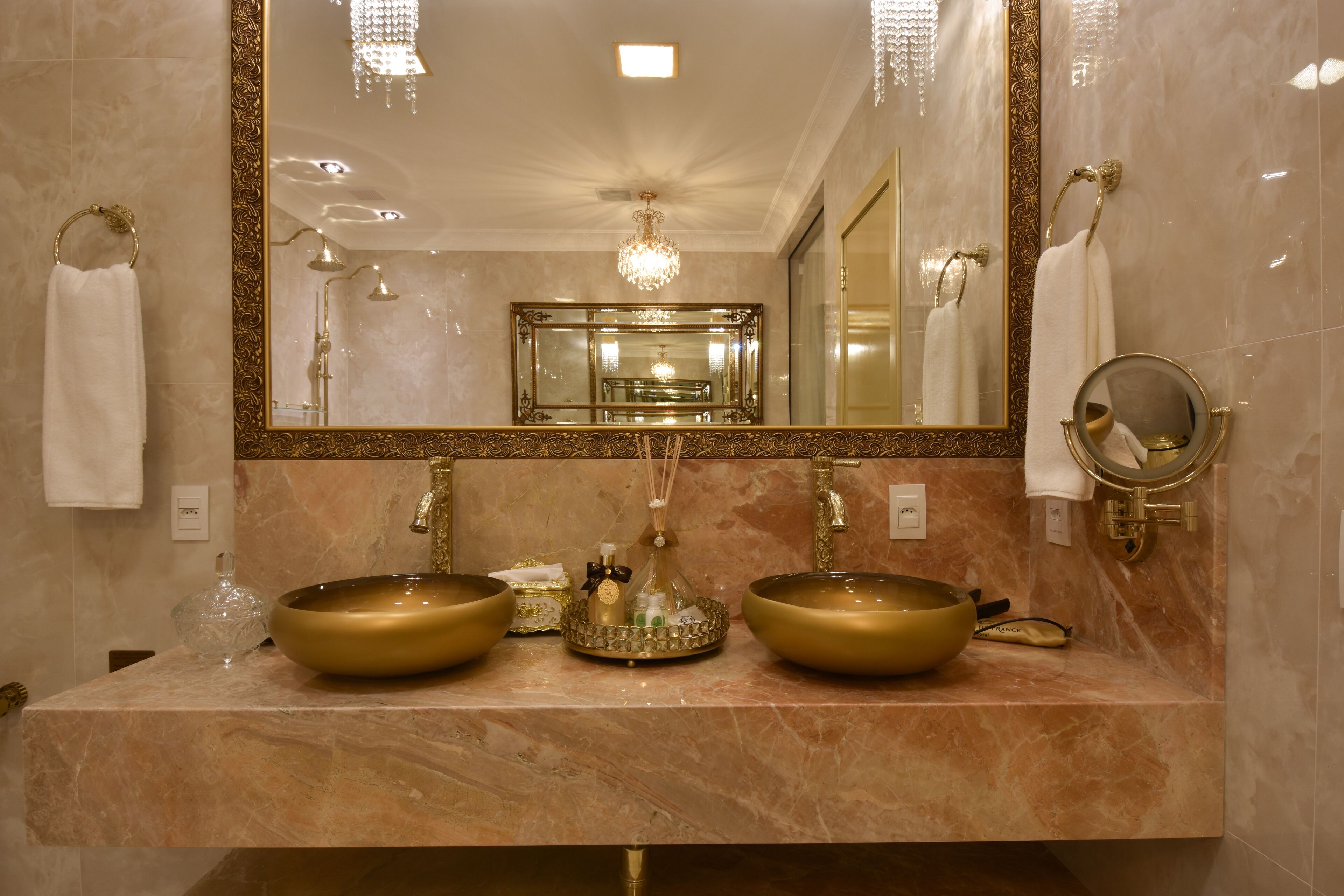 A bathroom with two gold sinks, a large mirror, and a chandelier.