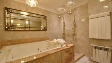 A luxurious bathroom with a large bathtub, a mirror with an ornate frame, a shower with a golden showerhead, and a towel rack with white towels.