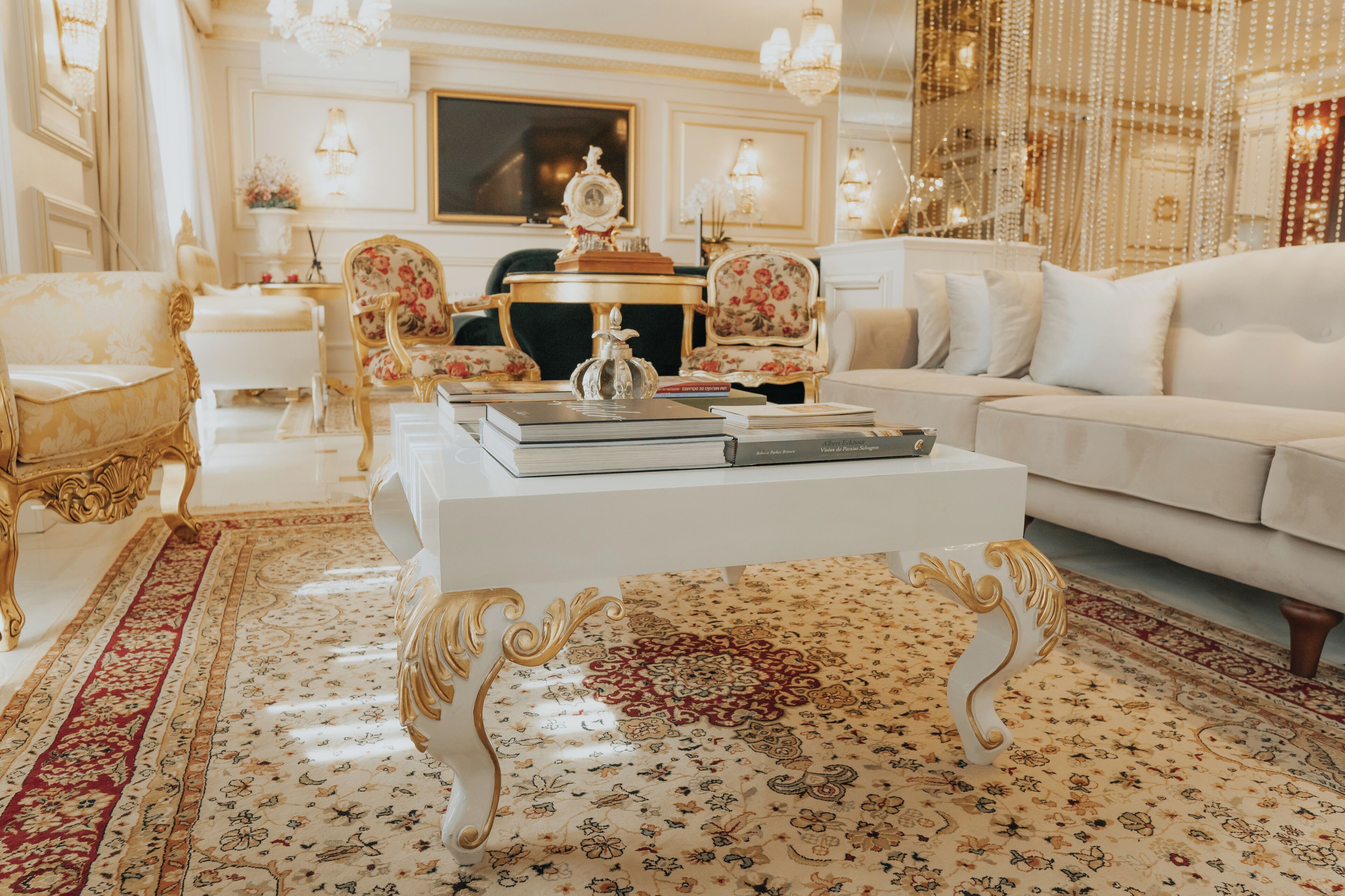 A luxurious living room with ornate furniture, a white sofa, and a coffee table with books.