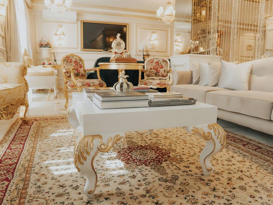 A luxurious living room with ornate furniture, a white sofa, and a coffee table with books.