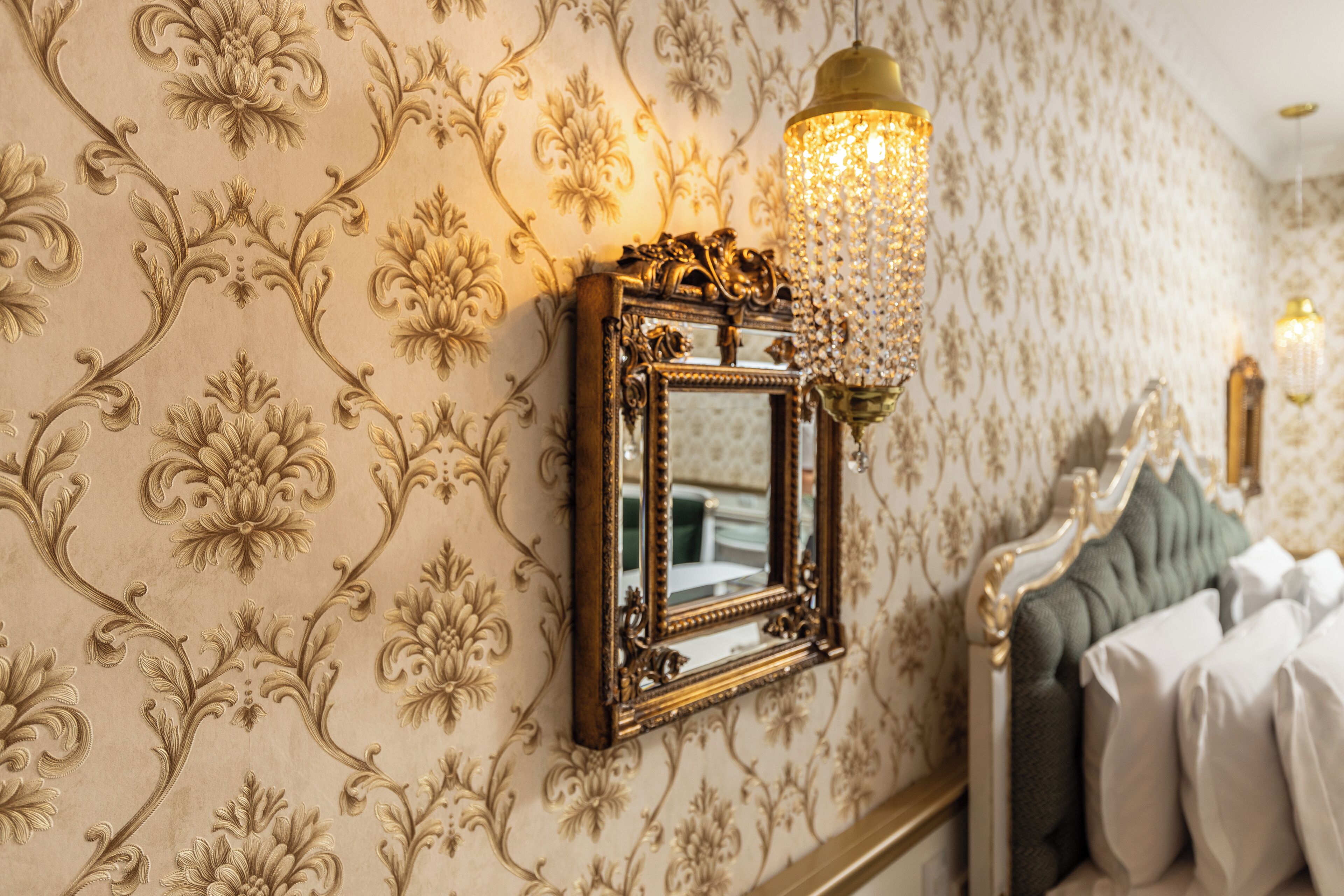 Una pared con papel tapiz floral decorativo, un espejo con marco dorado y una araña.