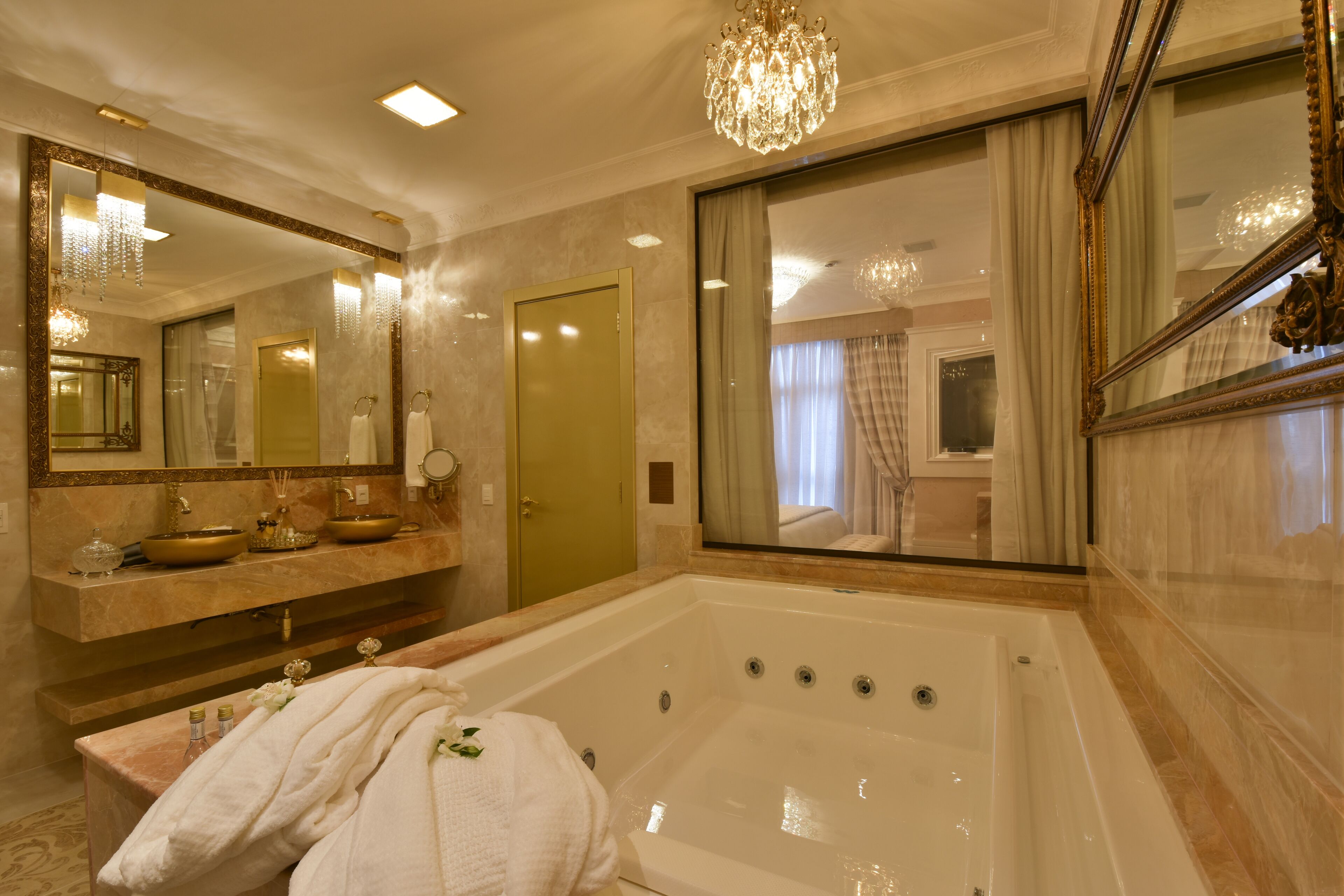 Un baño lujoso con una bañera grande, un tocador con un lavamanos dorado y un espejo amplio.