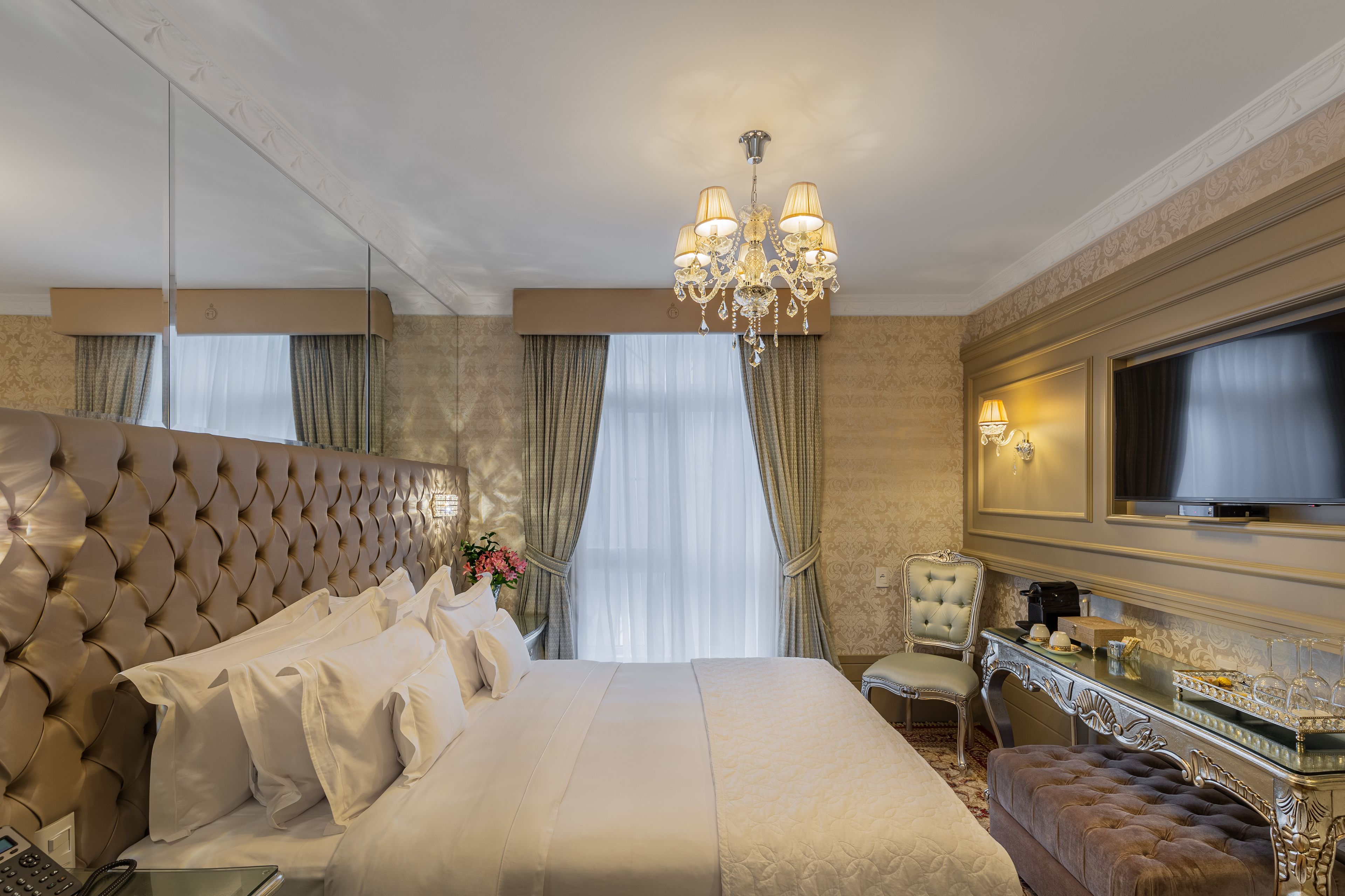 Una lujosa habitación de hotel con una cama grande, televisión, tocador con espejo y candelabro.