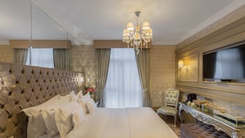 Una lujosa habitación de hotel con una cama grande, televisión, tocador con espejo y candelabro.