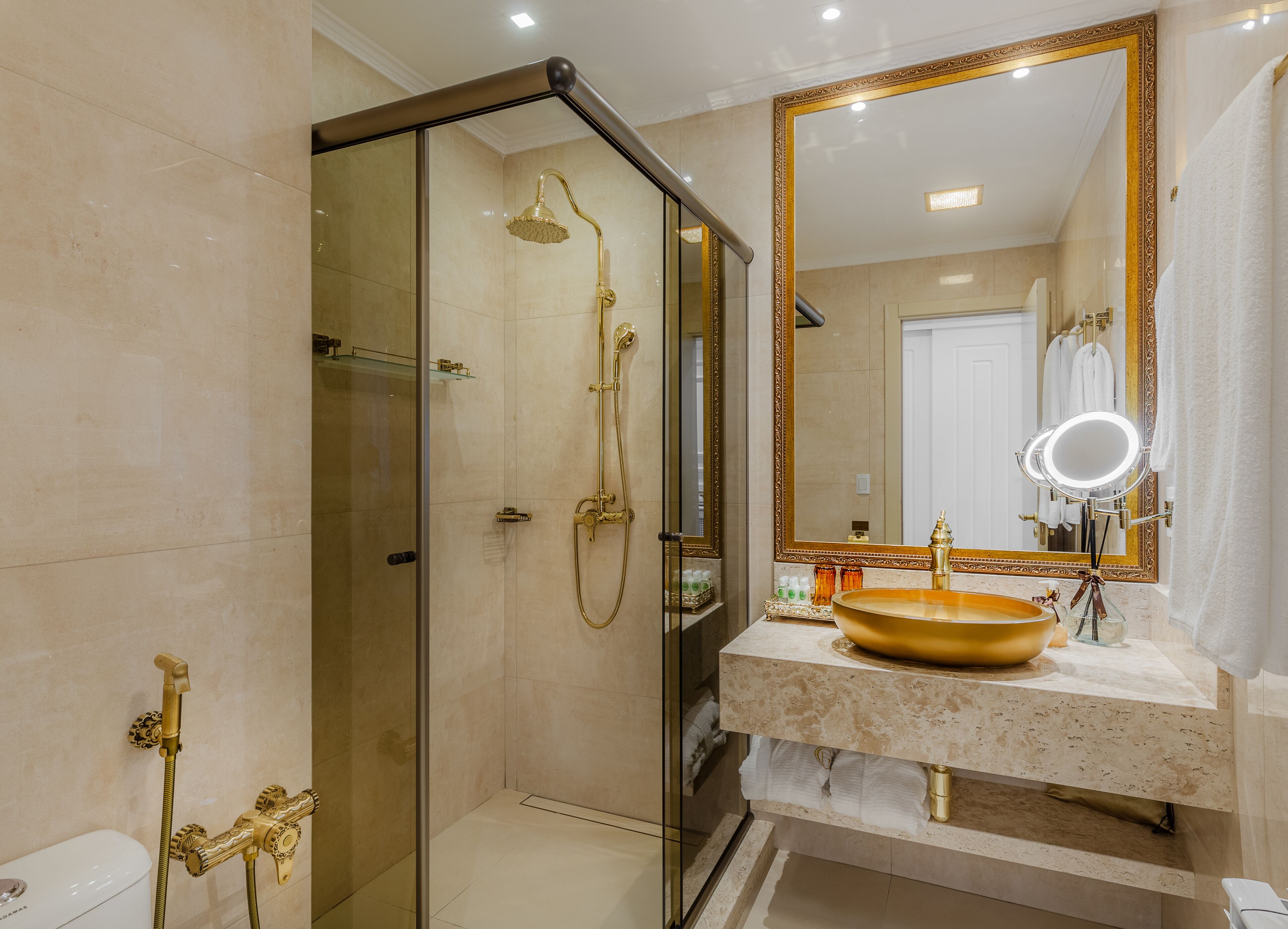 A luxurious bathroom with a gold shower, a large mirror, and a marble sink.