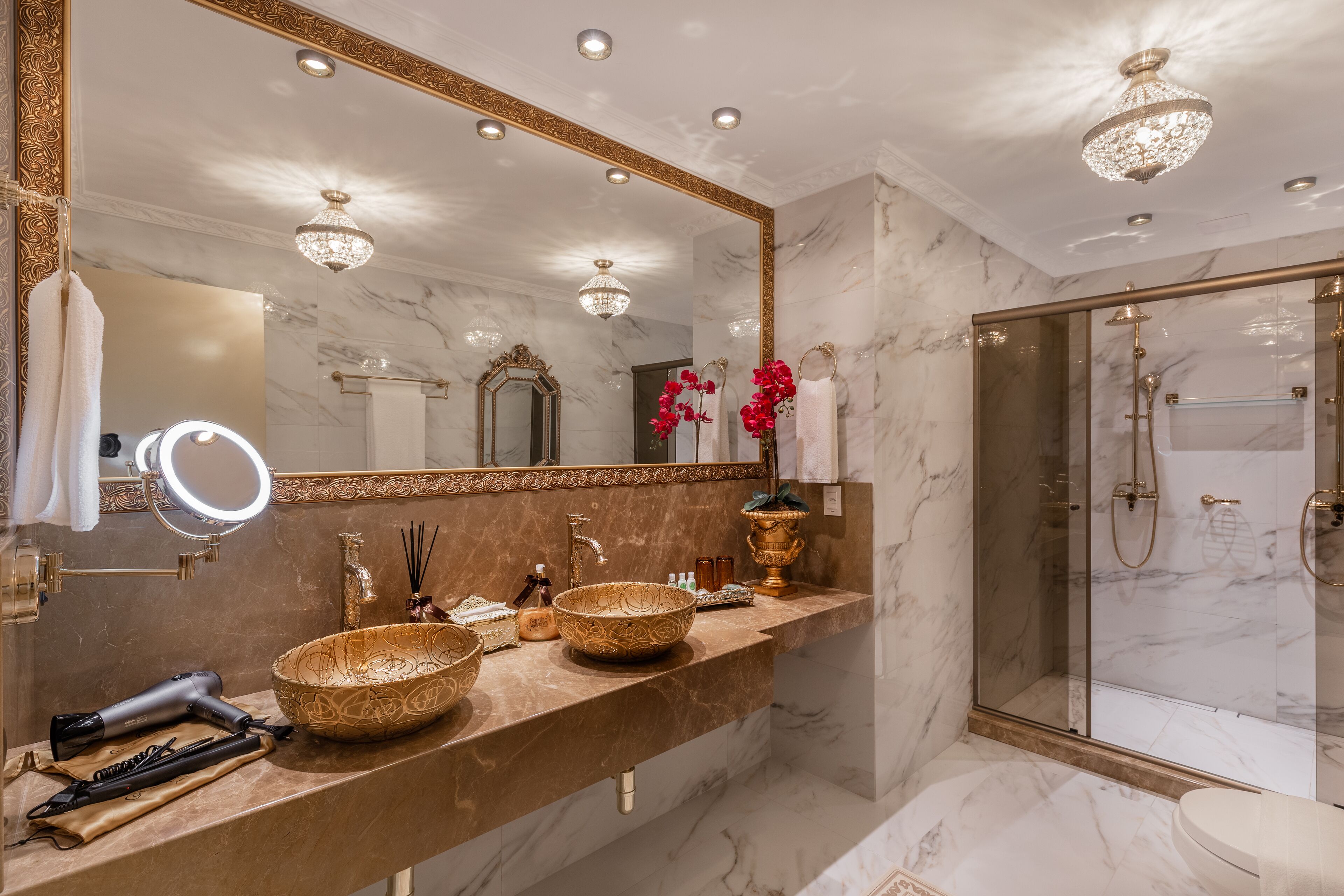 Une salle de bain luxueuse avec un meuble-lavabo en marbre, un grand miroir et une douche à l’italienne.