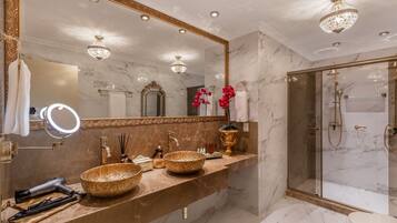 Une salle de bain luxueuse avec un meuble-lavabo en marbre, un grand miroir et une douche à l’italienne.