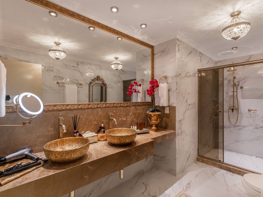 Une salle de bain luxueuse avec un meuble-lavabo en marbre, un grand miroir et une douche à l’italienne.