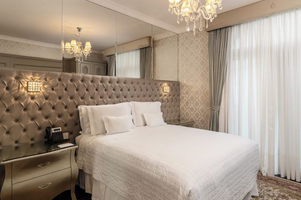 Ett hotellrum med en stoppad sänggavel, en telefon vid sängen, en sänglampa och en stor spegel.