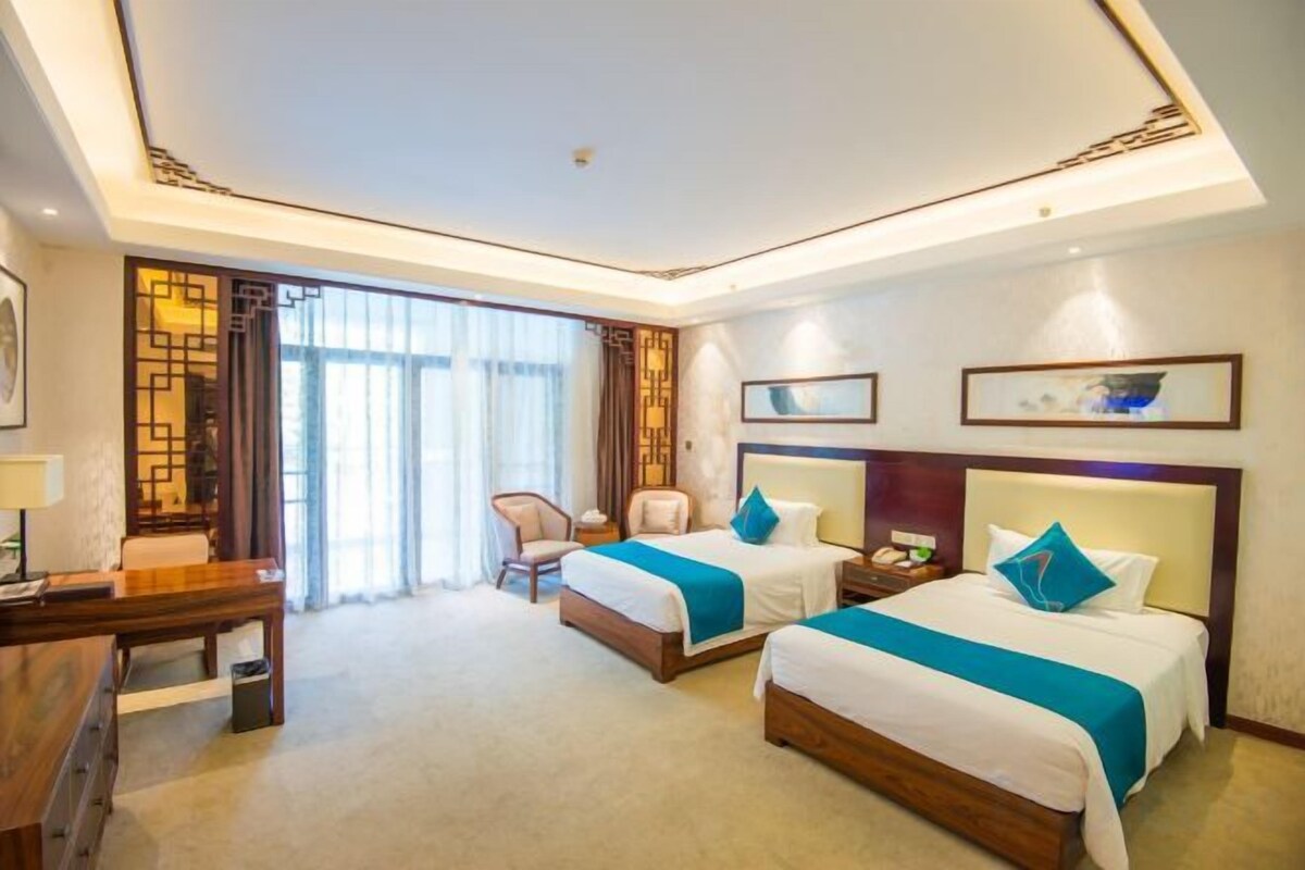A hotel room with two beds, a desk, a chair, and a large window.