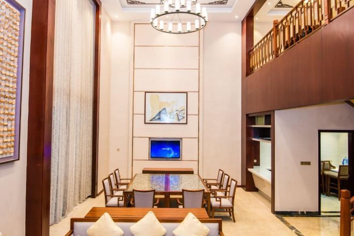 Een ruime lobby met een hoge plafond, een kroonluchter, een flatscreen televisie en een zithoek met een houten tafel en stoelen.