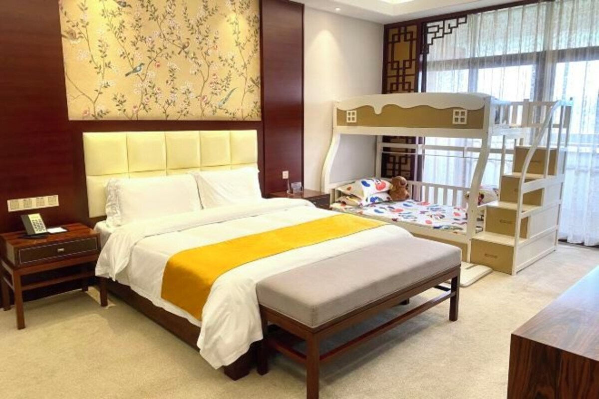 Une chambre d’hôtel avec un grand lit, un lit superposé, une table de chevet avec une lampe et un papier peint à motifs floraux.