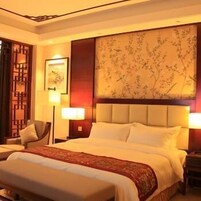 Una habitación de hotel con una cama grande, una mesita de noche con lámpara, una silla y un panel decorativo en la pared.