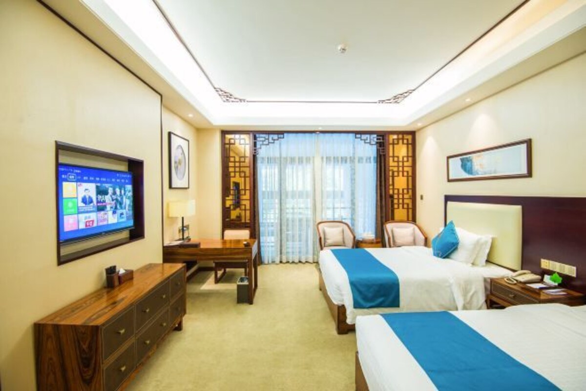 Une chambre d’hôtel avec deux lits, un bureau, une télévision et une fenêtre avec des rideaux.