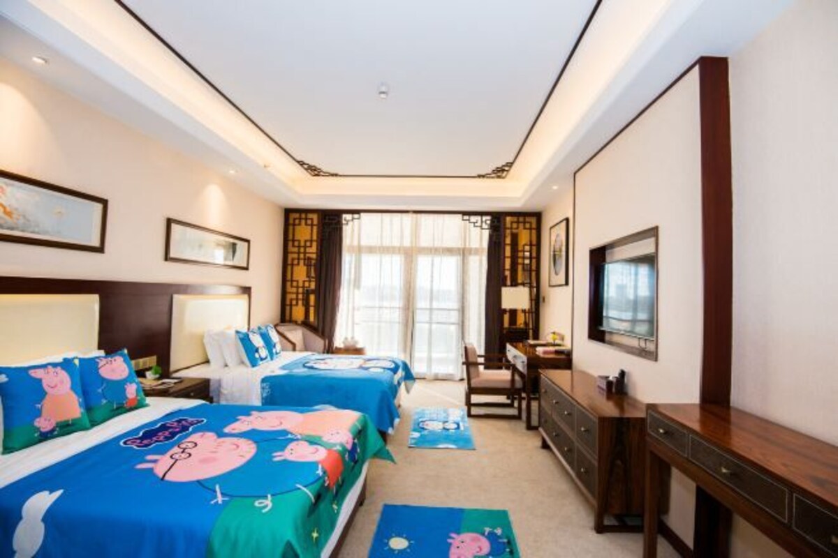 Une chambre d’hôtel avec deux lits, un bureau, une télévision et une fenêtre avec des rideaux.