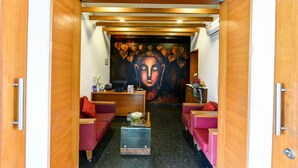 A reception area with a wooden reception desk, two red sofas, a coffee table, and a large Buddha mural on the wall. - Regenta Resort Soma Vine Village (Nashik)