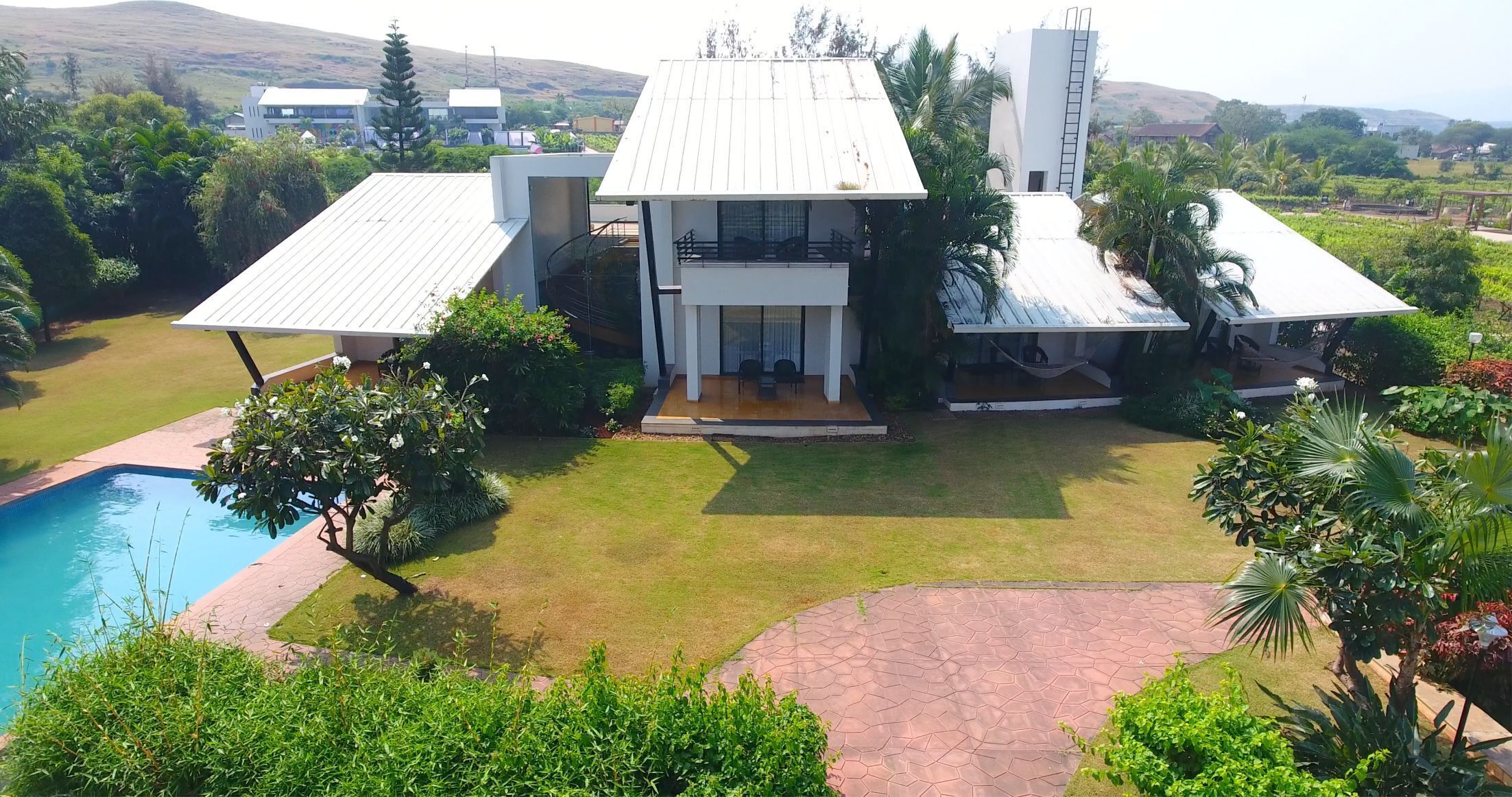 A modern house with a pool, surrounded by lush greenery and a hilly landscape.