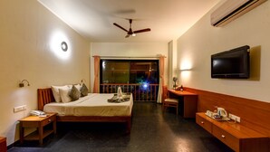 A hotel room with a bed, bedside table, desk, chair, TV, and a balcony with a view. - Regenta Resort Soma Vine Village (Nashik)