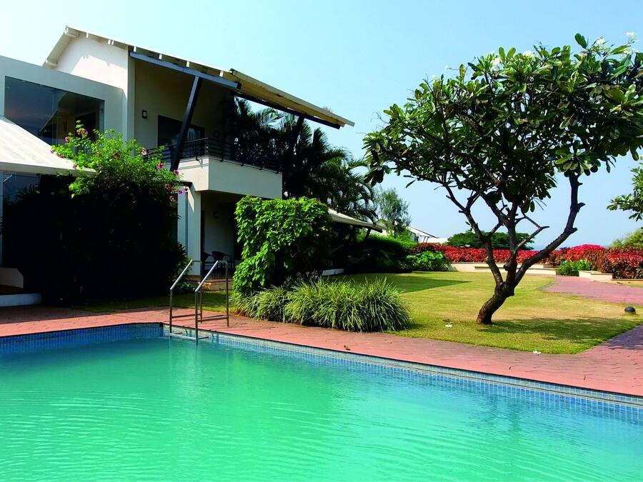A modern hotel with a swimming pool, a covered outdoor area, and lush landscaping.