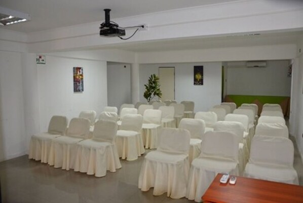 A conference room with rows of chairs and tables, a projector, and a plant. - Hotel Samaña (Arica)