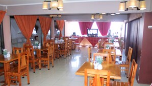 A restaurant with wooden tables and chairs, red curtains, and a television in the background. - Hotel Samaña (Arica)