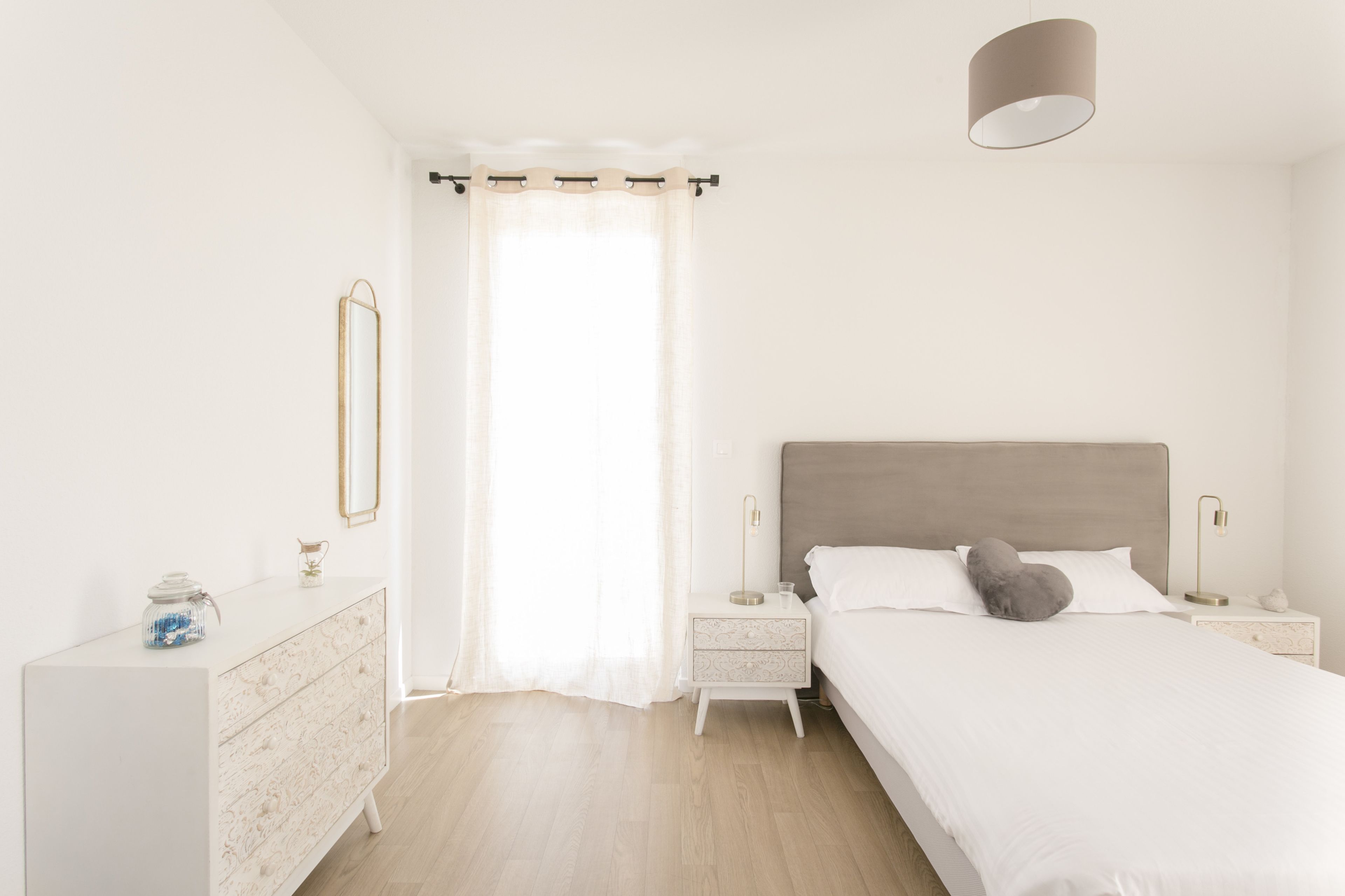Ein schlichter Schlafzimmer mit Bett, Nachttischen, einem Schminktisch und einem Spiegel.