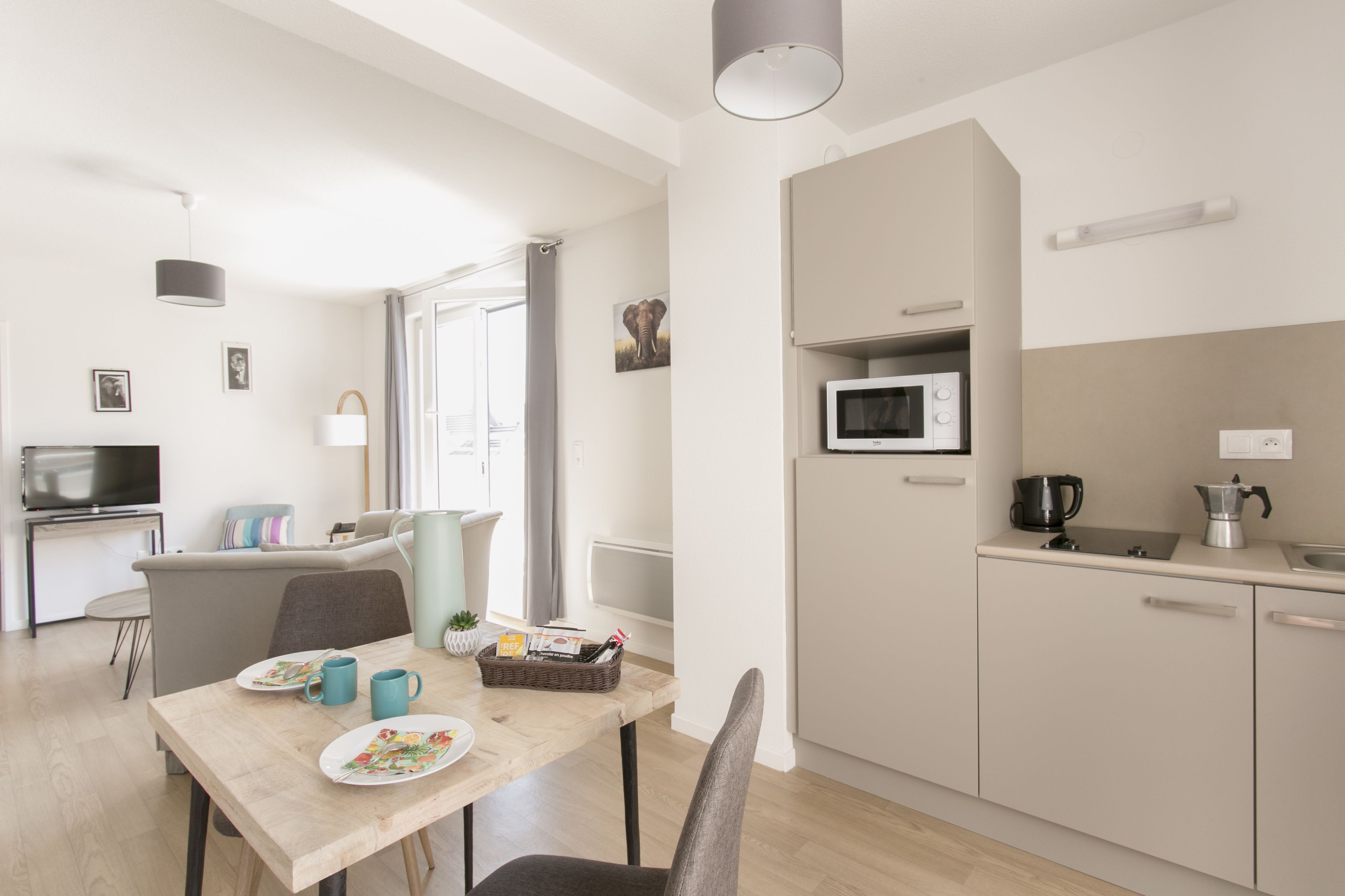 Une cuisine moderne équipée d’un four à micro-ondes, d’une bouilloire et d’un évier. Un coin repas est aménagé avec une table, des chaises et un panier rempli de magazines.
