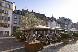 An outdoor café with tables and chairs, surrounded by cobblestone pavement and historic buildings. - Zenao Appart'hôtels Mulhouse (Mulhouse)