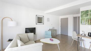 En moderne stue med sofa, et rundt bord, fjernsyn, et skab og en stol.