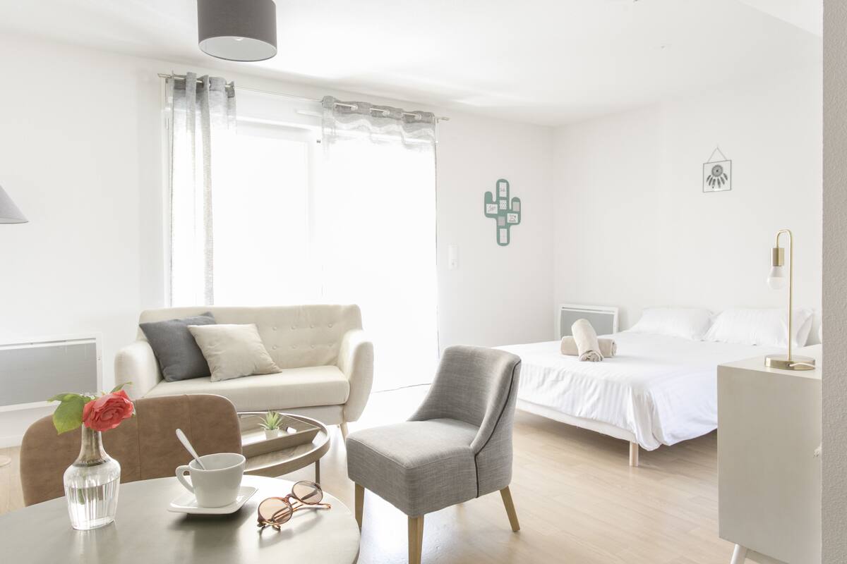 Een moderne hotelkamer met een bed, een bank, een stoel, een klein tafeltje met een kopje en glazen, en een vaas met een bloem.