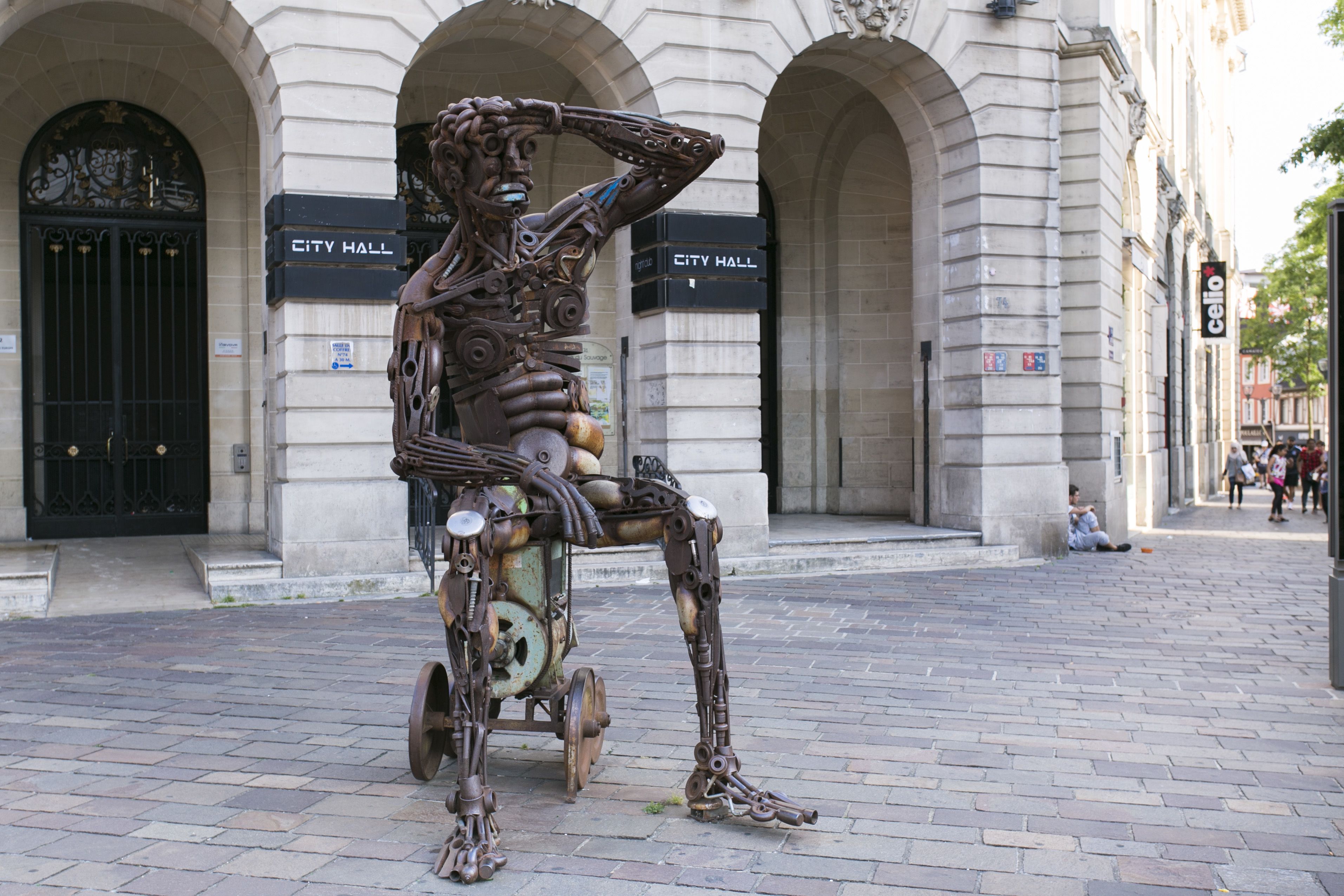 A sculpture of a human figure made from mechanical parts in front of City Hall.