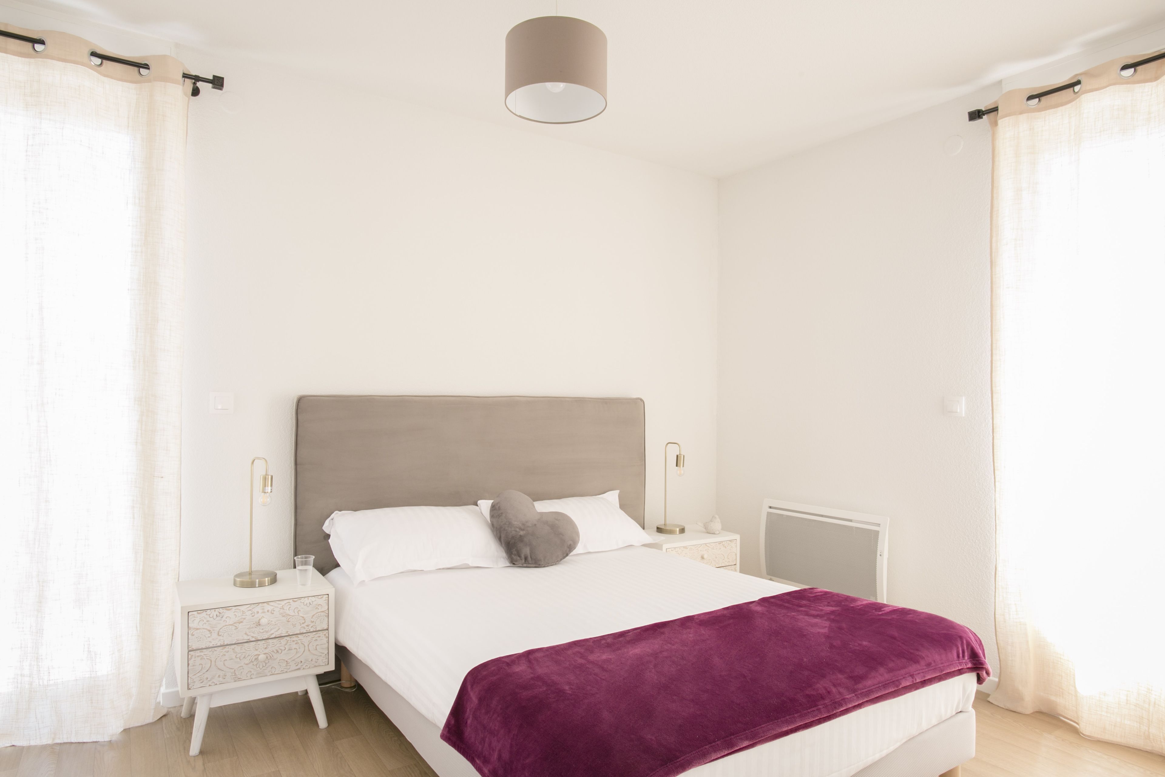 A modern bedroom with a bed, nightstands, a lamp, and a radiator.