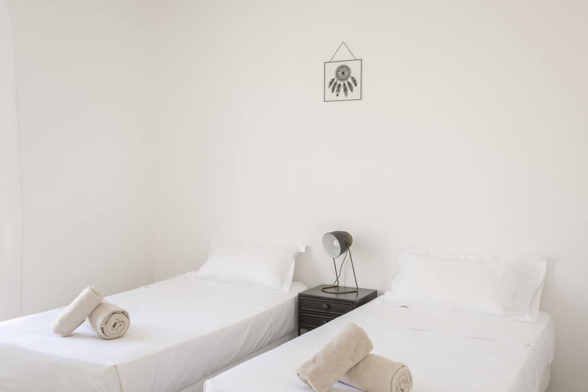 Een hotelkamer met twee enkele bedden, een nachtkastje met een lamp en een wandklok.