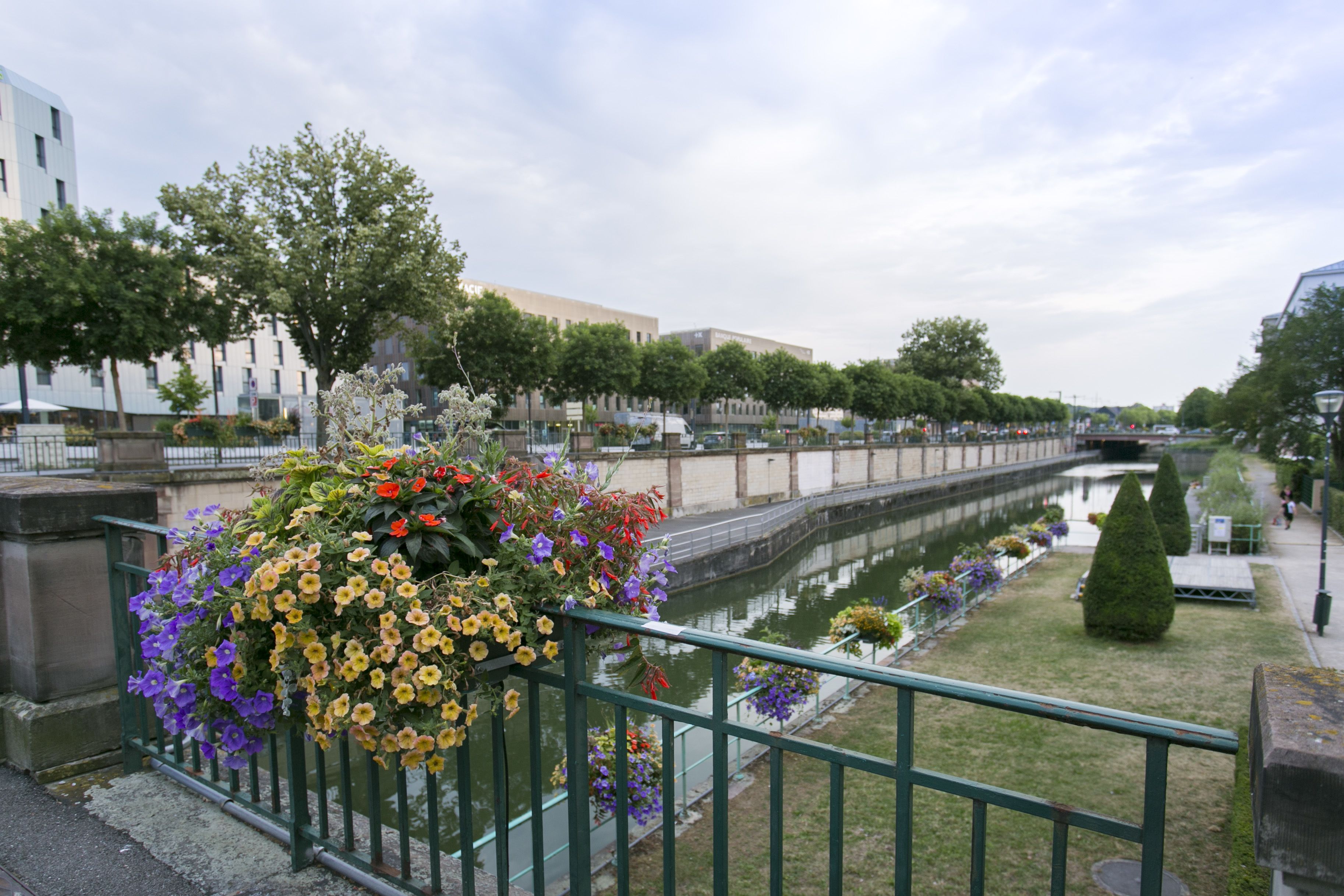A canal with flower baskets on the railing, a bridge, and buildings along the water.