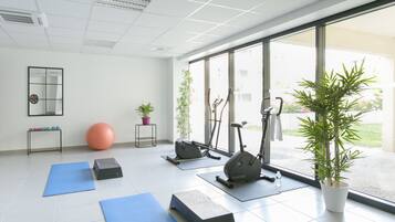 A spacious room with exercise equipment, including an elliptical and a stationary bike, and a large potted plant.