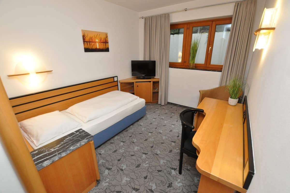 Una habitación de hotel con cama, escritorio, televisor y ventana con cortinas.