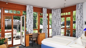 Un dormitorio con cama, escritorio y silla, ventanas amplias con cortinas y vistas al exterior.