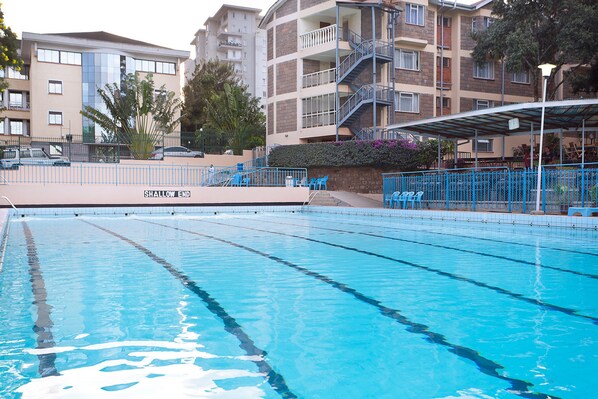 A swimming pool with clear lanes, surrounded by a fence and a covered seating area.