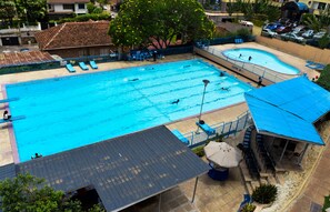 A large outdoor swimming pool with multiple lanes, surrounded by lounge chairs and a covered seating area. - Methodist Resort (Nairobi)