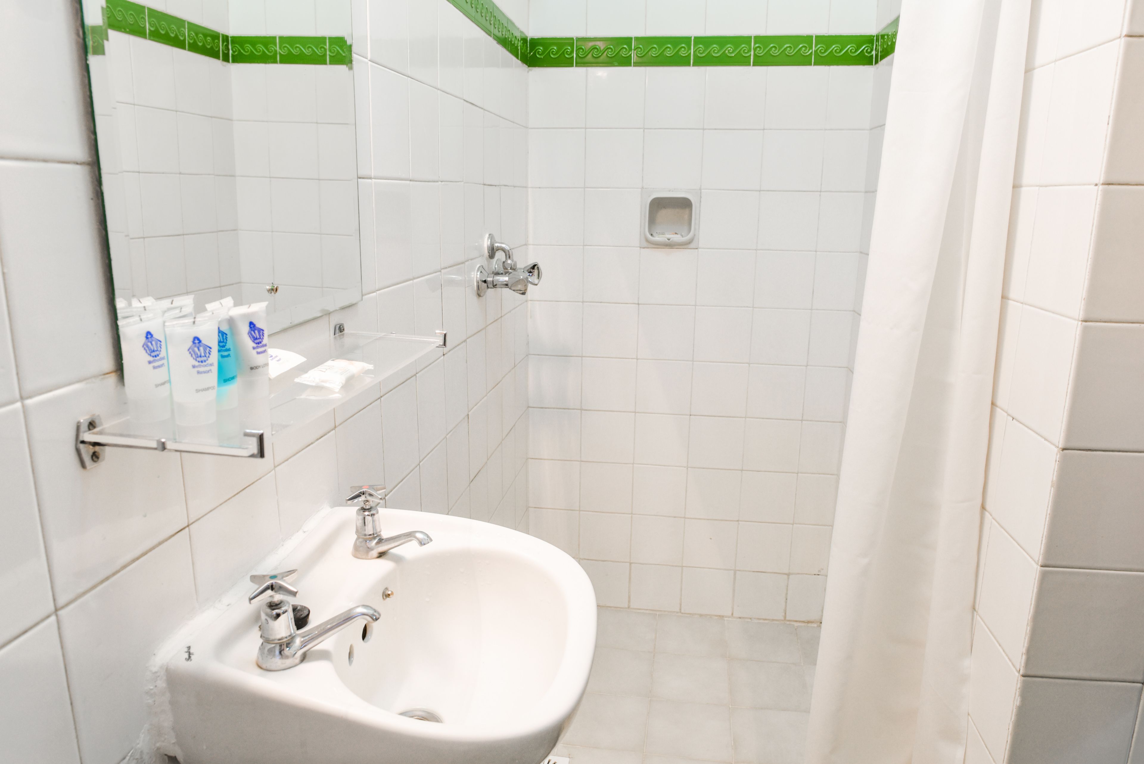 A bathroom with a white sink, mirror, and green-tiled shower area.