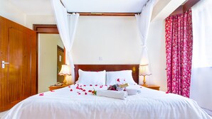 A neatly made bed with white linens and rose petals, two bedside lamps, and a wooden headboard. - Methodist Resort (Nairobi)