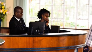 A reception desk with a wooden finish and a computer monitor. - Methodist Resort (Nairobi)