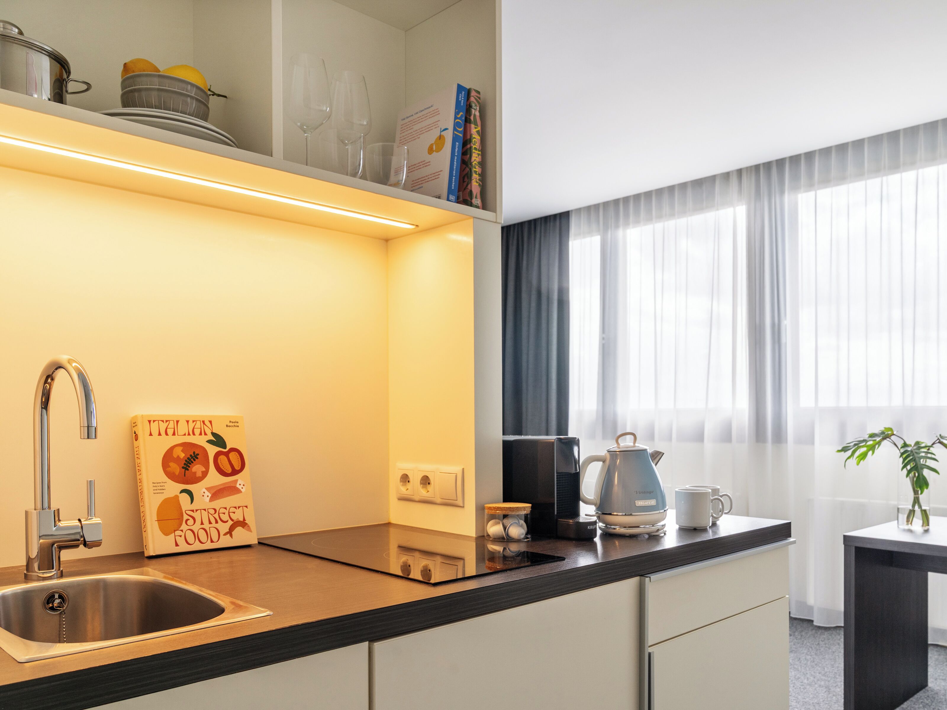 A modern kitchen with a stainless steel sink, a kettle, and a coffee maker on the countertop.