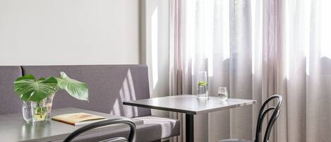 A modern dining area with a grey sofa, two black chairs, a glass table, and a potted plant.